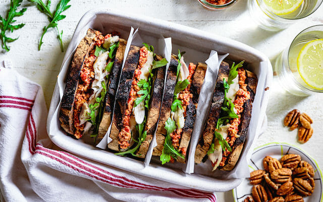 Rotisserie chicken sandwich with muhammara and arugula in white ceramic dish