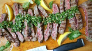 Skirt steak with salsa verde sliced on a cutting board with lemon garnish