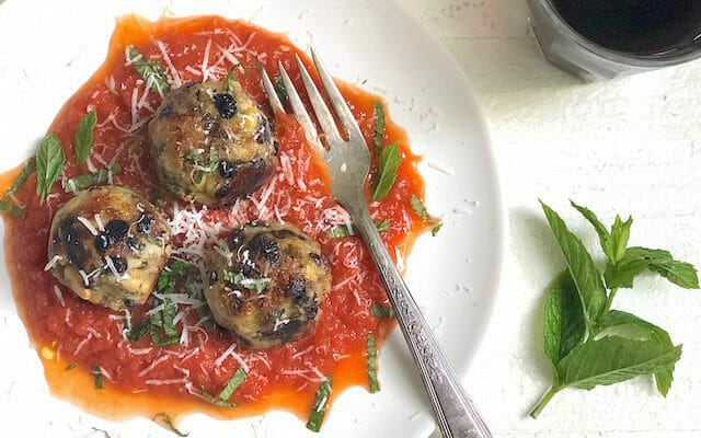 vegan meatballs made with eggplant and tempeh on a white plate with red sauce and a fork