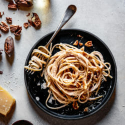 Linguine alfredo on a dark plate with a fork, parmesan, and pecans