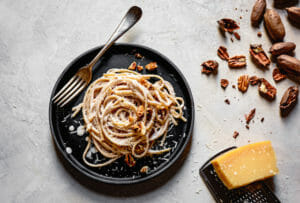 Linguine alfredo on a dark plate with a fork, parmesan, and pecans