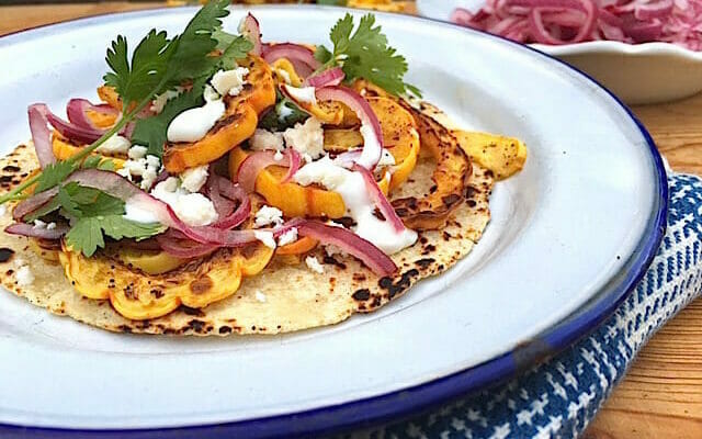 delicata squash tacos topped with cilantro and sour cream on a white plate with a blue and white napkin