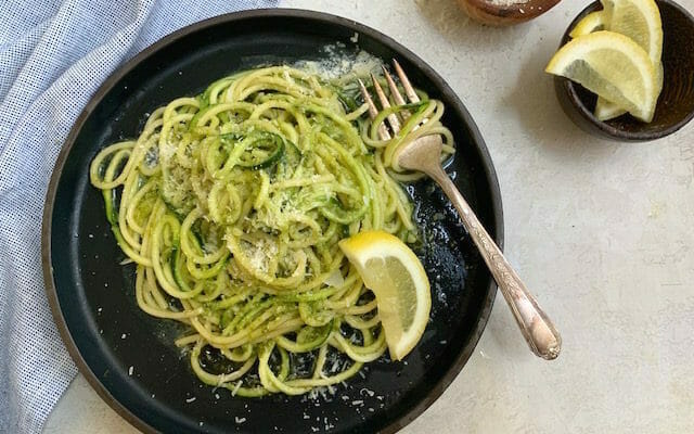 Spaghetti and zucchini noodles with pesto on a dark plate with a fork