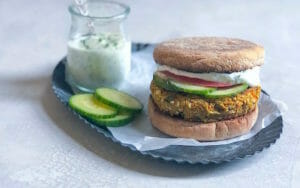 Falafel burgers on a bun with cucumbers and tomato and a jar of yogurt sauce