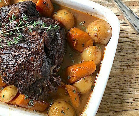 pot roast in a white dish with carrots and potatoes