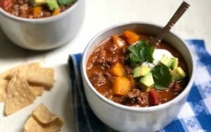 bowl of beef and butternut squash chili topped with avocado and cilantro with some tortilla chips
