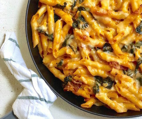 close up of baked pumpkin pasta in a cast iron skillet with a dish towel