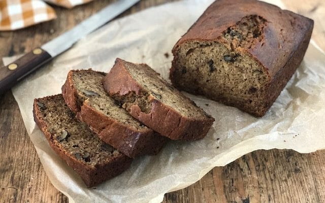 Thick slices of banana walnut bread on a piece of parchment with a bread knife and a checked cloth