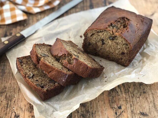 Thick slices of banana walnut bread on a piece of parchment with a bread knife and a checked cloth