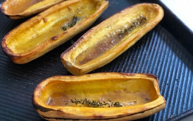 Halved Roasted Delicata Squash on a sheet pan with thyme, maple syrup, and butter