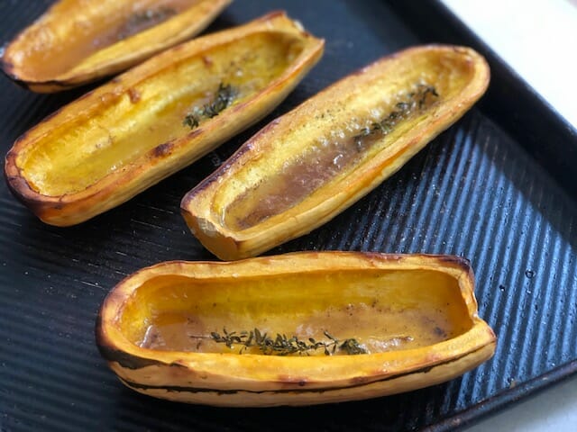 Halved Roasted Delicata Squash on a sheet pan with thyme, maple syrup, and butter