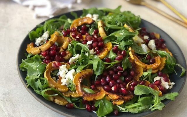 Beautiful Arugula, delicata squash, and pomegranate salad in a large shallow bowl on white background