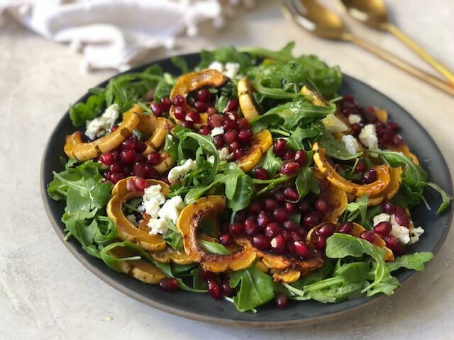 Beautiful Arugula, delicata squash, and pomegranate salad in a large shallow bowl on white background