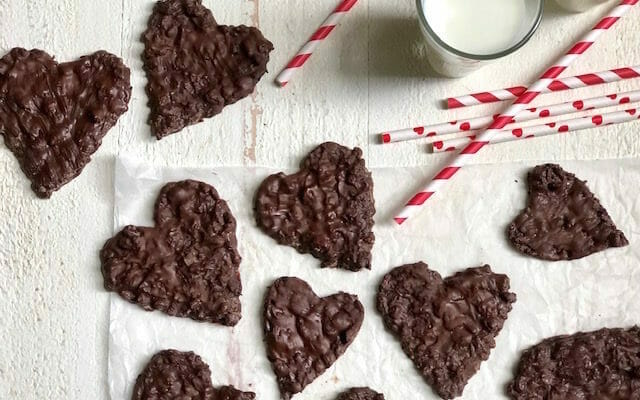 Heart shaped chocolate coconut treats on a white background with milk and red and white paper straws