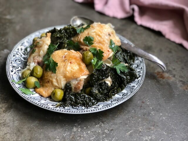 Instant pot chicken thighs olive and kale on a black and white plate and pink napkin