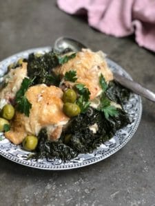 Chicken and olives and kale on a vintage black and white plate with a pink napkin