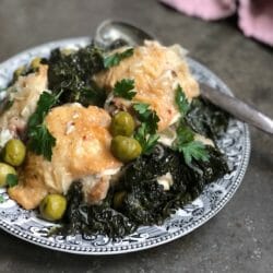 Chicken and olives and kale on a vintage black and white plate with a pink napkin