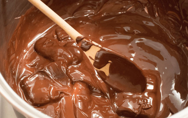 Big metal bowl of melted chocolate with a wooden spoon and 12 chocolate recipes