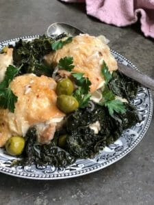 Chicken thighs with olives and kale on a vintage black and white plate with a pink napkin