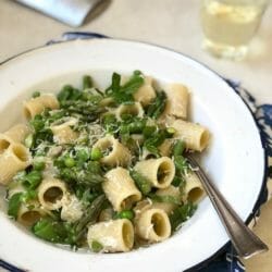 Bowl of pasta with asparagus, peas, and lemon in a white bowl with a glass of white wine.