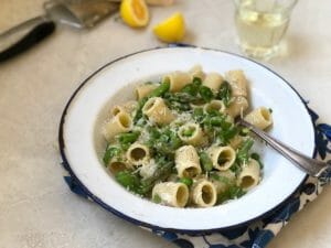 White bowl with rigatoni pasta, asparagus, peas, with white wine and a half lemon
