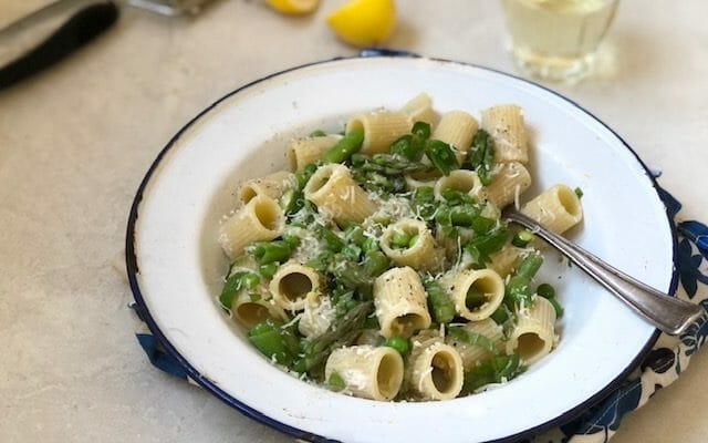 White bowl with rigatoni pasta, asparagus, peas, with white wine and a half lemon