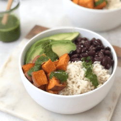 white bowl with rice, black beans, sweet potatoes and avocado with a green sauce