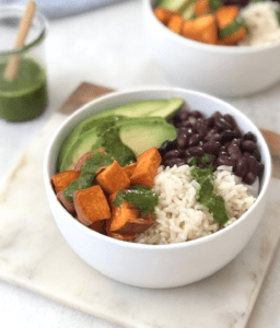 white bowl with rice, black beans, sweet potatoes and avocado with a green sauce