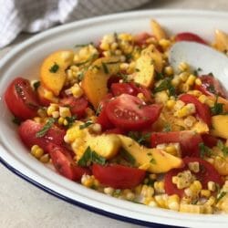 Peach, tomato, and corn salad on a white platter with a white spoon