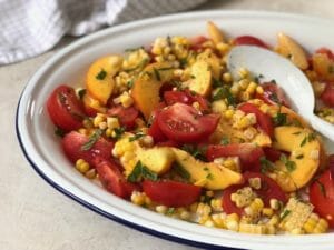 Peach, tomato, and corn salad on a white platter with a white spoon