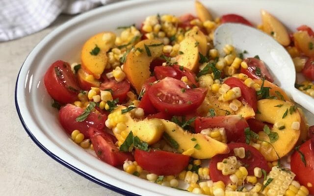 Peach, tomato, and corn salad on a white platter with a white spoon