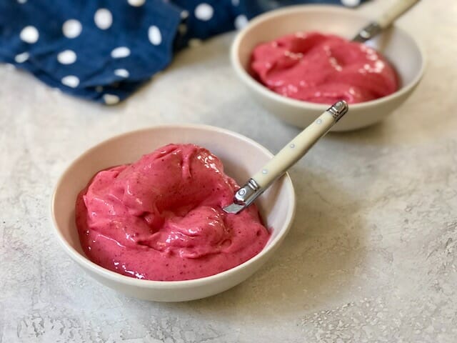 Two bowls of homemade raspberry sorbet with spoons and a navy polka dot napkin