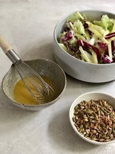 bowl of lettuce, vinaigrette, and bowl of seeds for salad