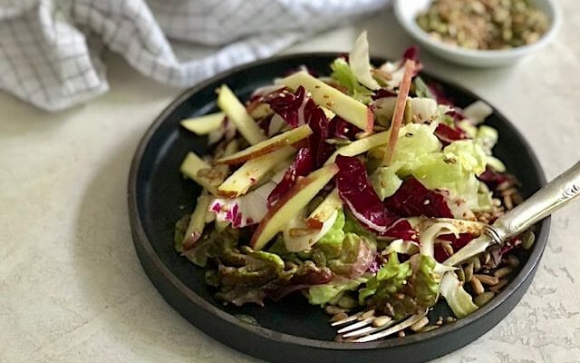 Salad of apple and lettuce on a dark plate with a side of seeds