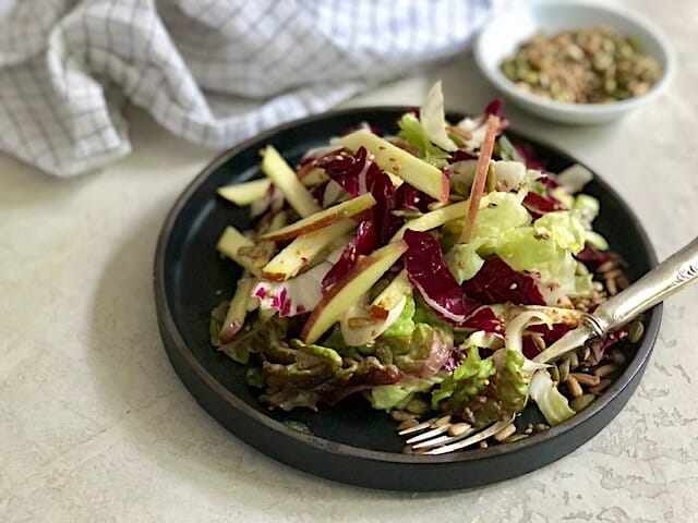 Salad of apple and lettuce on a dark plate with a side of seeds