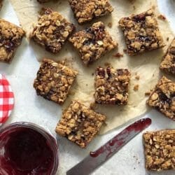 Jammy oatmeal crumble bars with an open jar of raspberry jam