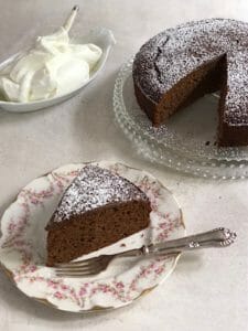 Wedge of gingerbread cake with bowl of whipped cream