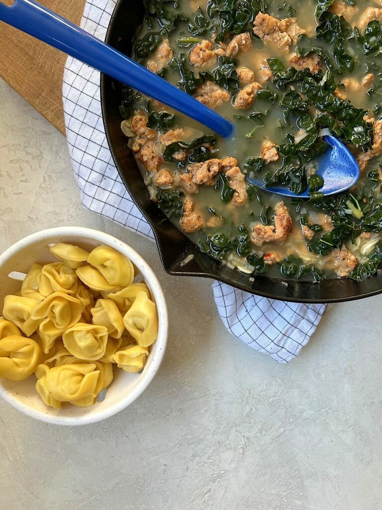 Pan of brothy sausage and kale with tortellini