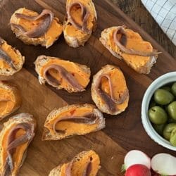 Little toasts with anchovy and butter on a wooden board with olives and radishes