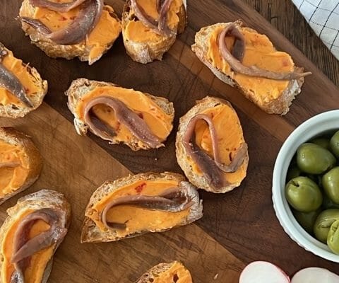 Little toasts with anchovy and butter on a wooden board with olives and radishes