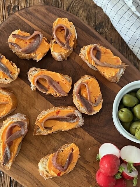 Little toasts with anchovy and butter on a wooden board with olives and radishes