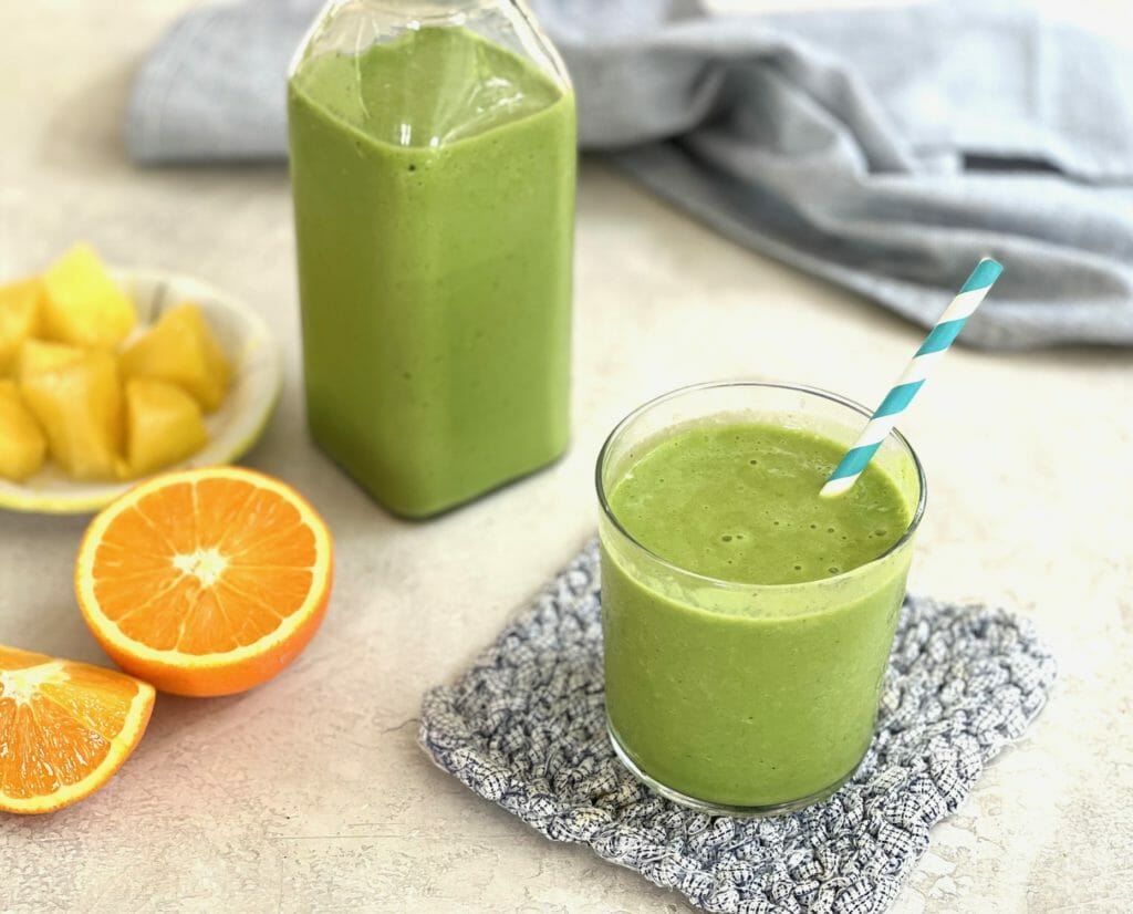 A glass and a jug of pineapple orange green smoothie