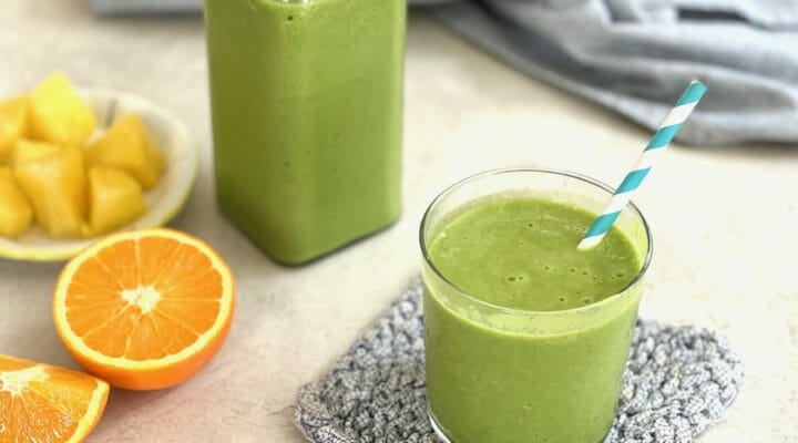 A glass and a jug of pineapple orange green smoothie