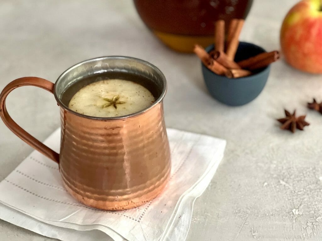 Copper mug of bourbon-spiked cider with apple garnish