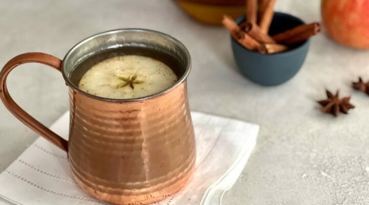 Copper mug of bourbon-spiked cider with apple garnish